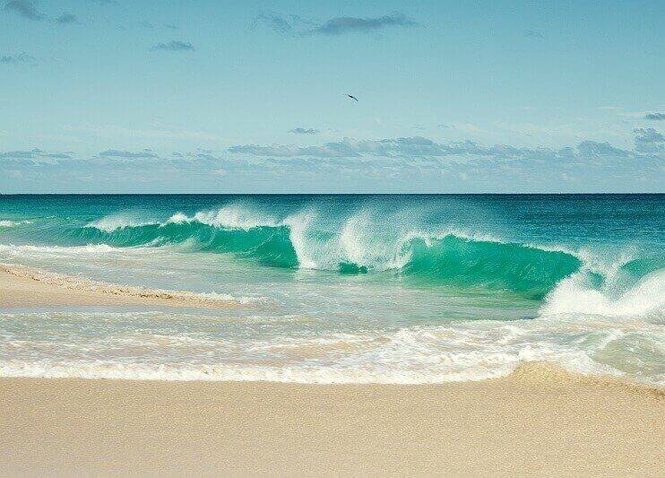 Hohe Wellen brechen am hellen Sandstrand auf den Kapverden bei türkisblauem Meer.